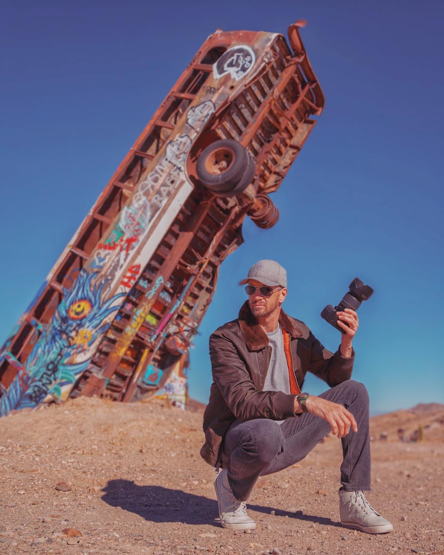 man crouching in front of a bus holding a camera