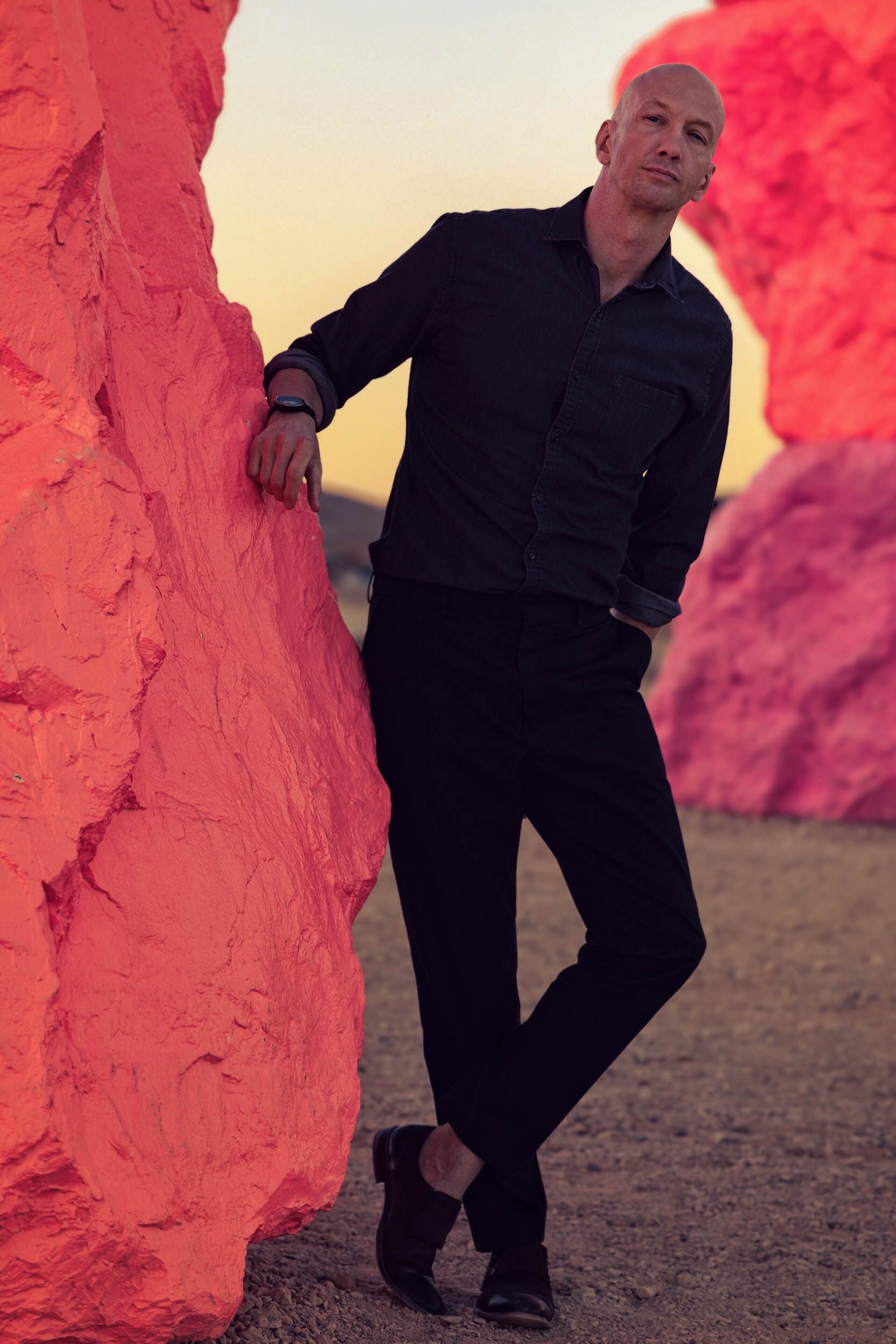 a man in black dress clothes leaning against a pink rock for a tinder photo