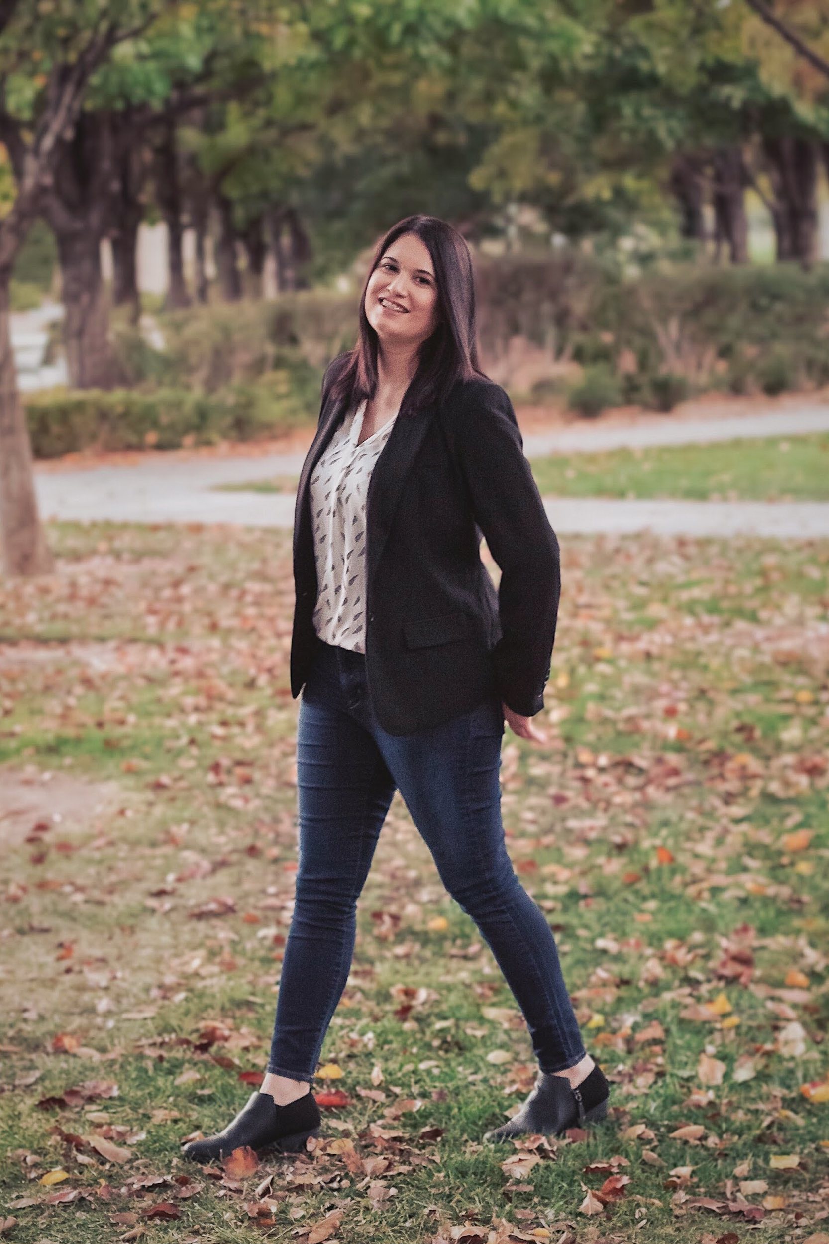 a smiling woman in jeans & a black blazer walking in grass