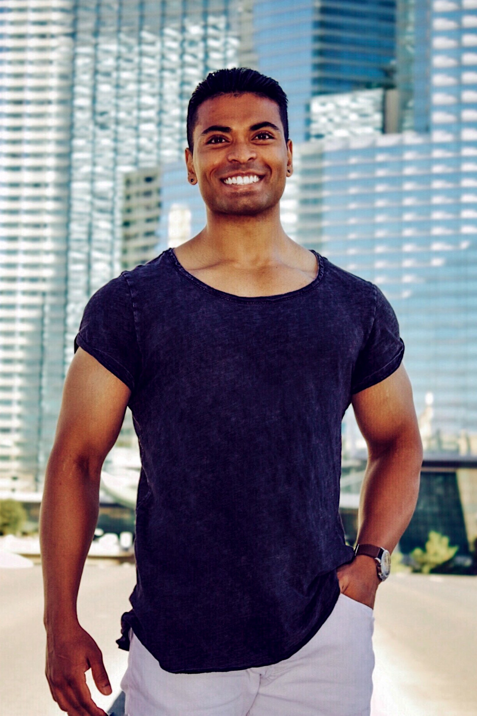 a smiling guy in a black shirt standing in front of a glass building.