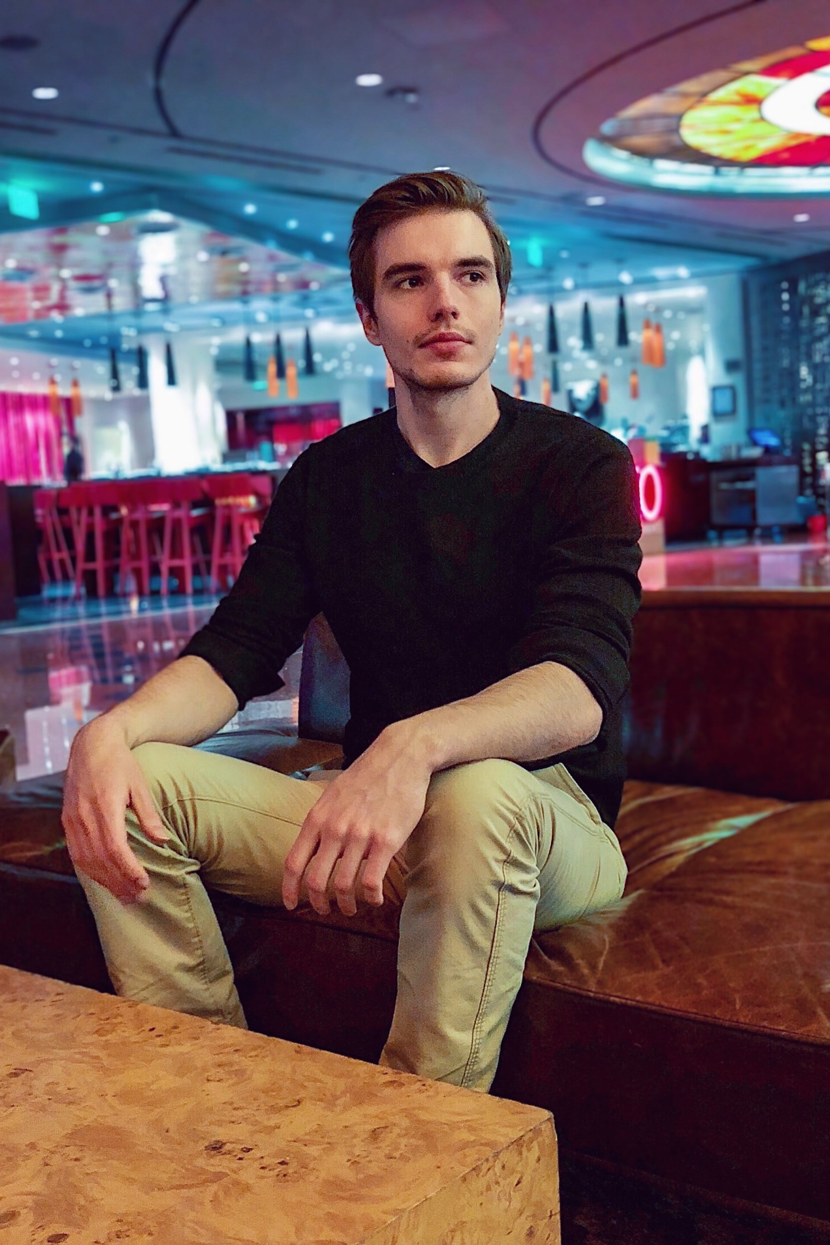 man in black sweater & tan pants sitting in a lounge.