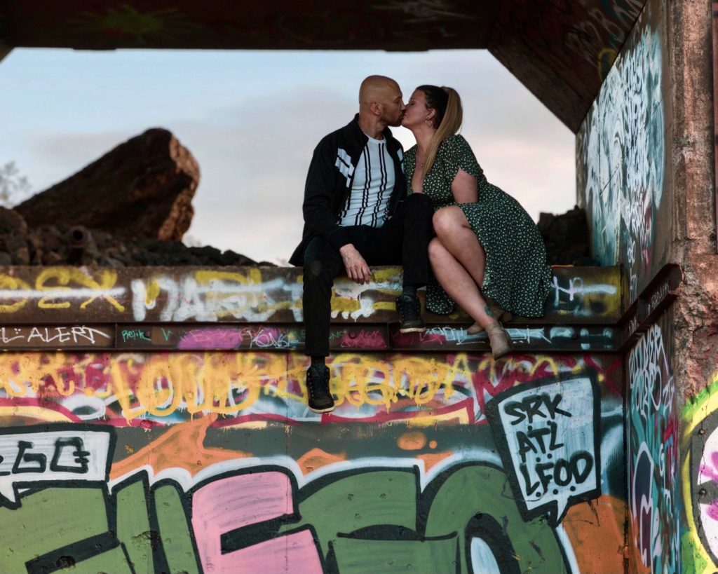 a man & woman kissing on a graffiti covered concrete structure near a mine.