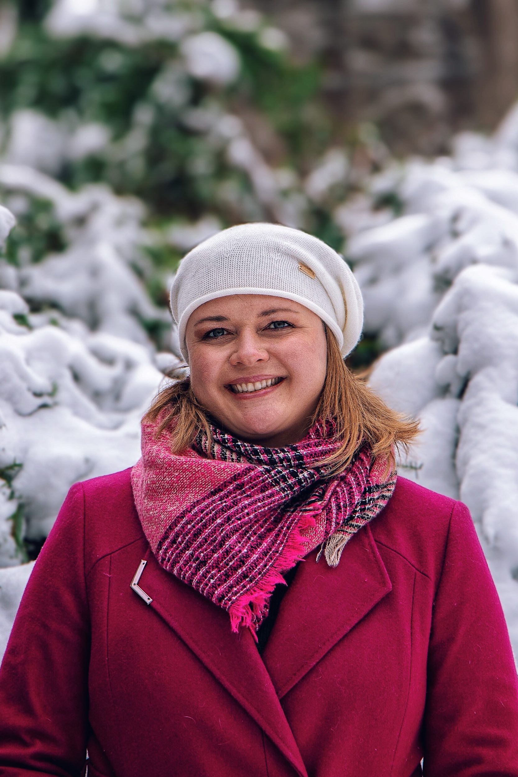 a smiling woman in pink jacket & beret outside in the snow.