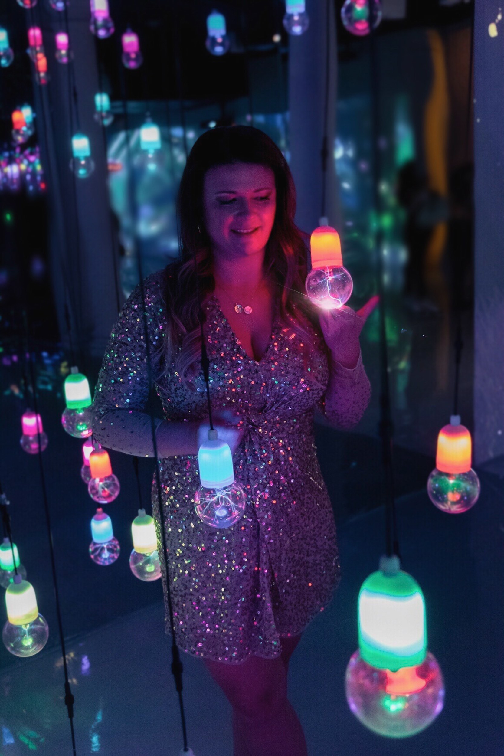 woman in a sequined dress touching a colored lightbulb.