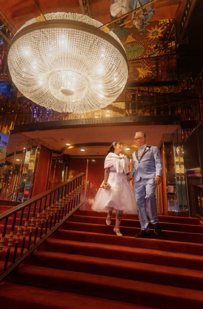 A newlywed couple in vintage attire share a look as they walk down the stairs of a downtown Las Vegas casino.