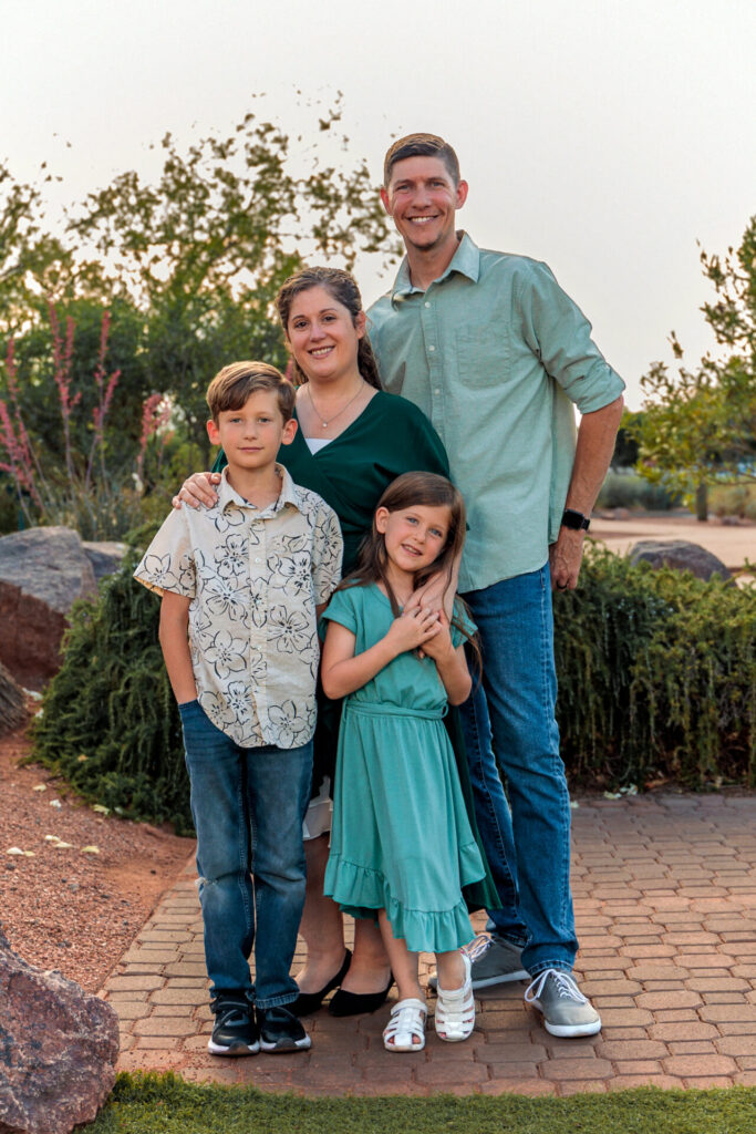 A family of four poses together in a Las Vegas park for a professional outdoor portrait, wearing green & grey color coordinated outfits.