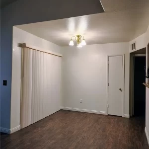 A dimly lit corner of a condo with white walls & a wood floor, taken by a real estate agent.