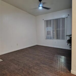 A dimly lit empty condo living room with one window & a ceiling fan.