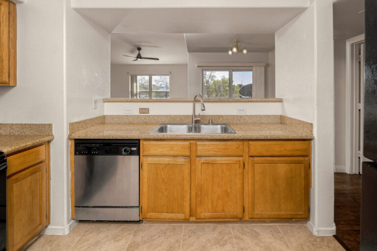 Kitchen of a condo with stainless steel appliances & wood cabinets & beige tile floor.