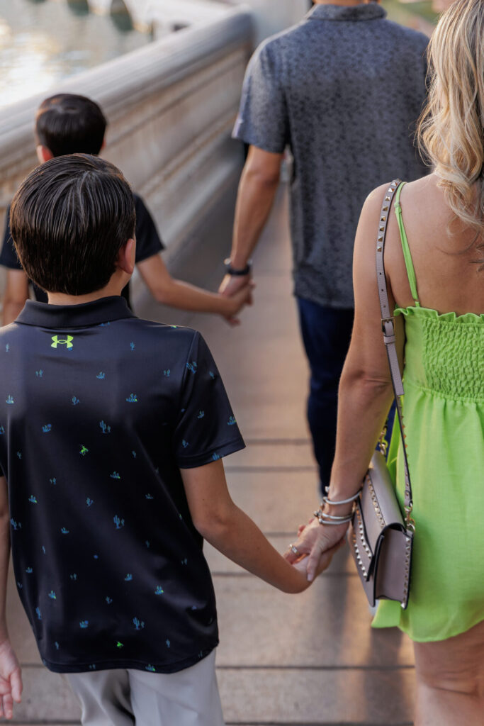 A close up view from behind of a family walking hand in hand along the Las Vegas Strip, showing the parents and children holding hands during a candid photo.