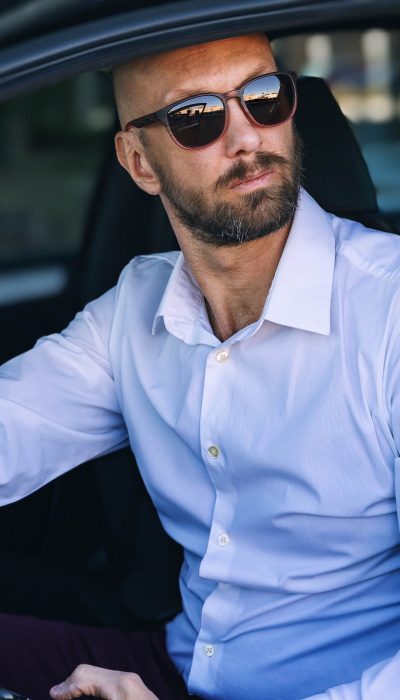 a man in a white dress shirt and sunglasses sitting in a car holding his phone