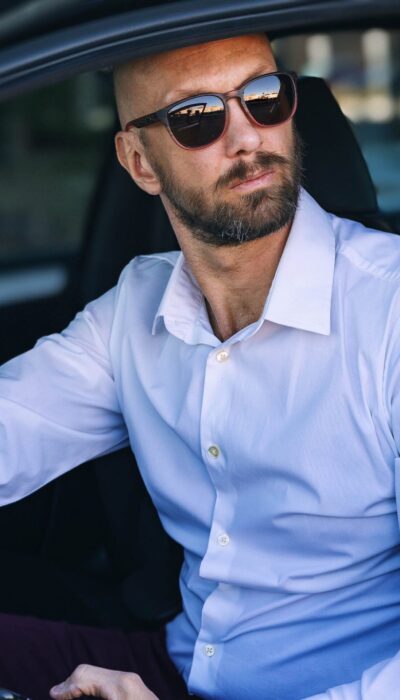 a man in a white dress shirt and sunglasses sitting in a car holding his phone