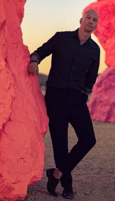 a man in black dress clothes leaning against a pink rock for a tinder photo