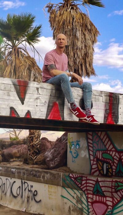 a guy in a pink t shirt sitting own a bridge thats covered in graffiti.